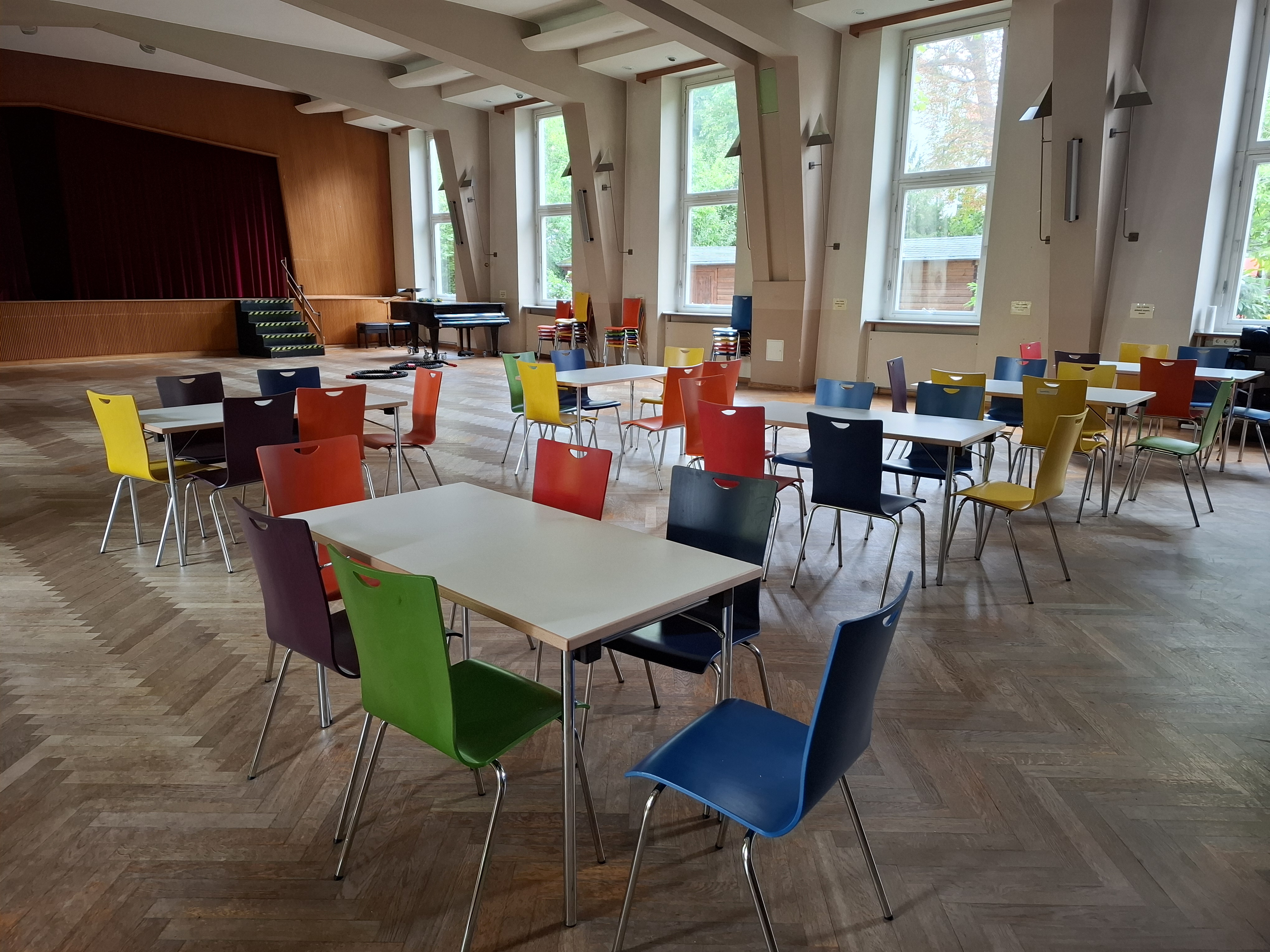 Blick in den großen Saal mit Tischen und bunten Stühlen
